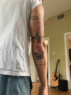 a man with a tattoo on his arm standing in a living room next to a guitar