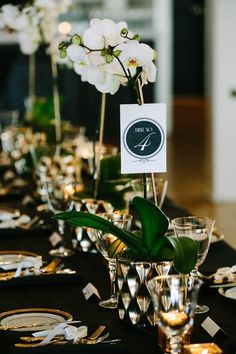 the table is set with silver and black place settings, white orchids in glass vases