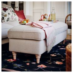 a white ottoman sitting on top of a rug next to a table with tea cups