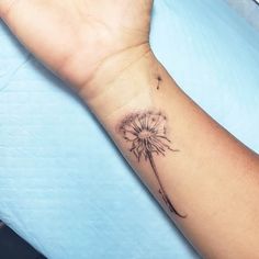 a woman's arm with a dandelion tattoo on the left side of her wrist