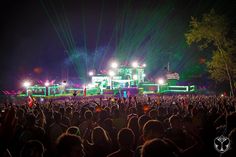 a large group of people standing in front of a stage with lights on it at night