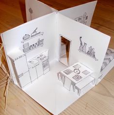 an open book with drawings on it sitting on top of a wooden table next to a pair of scissors