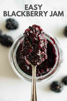 a spoon full of blueberry sauce with berries around it and on top of the jar