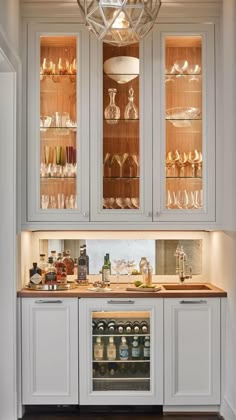 a kitchen with white cabinets and glass shelves filled with wine bottles, glasses, and other condiments