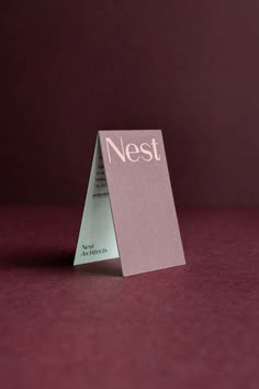 a folded card with the word nest on it sitting in front of a red background