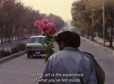 a man is walking down the street with flowers in his hand and cars on the road behind him