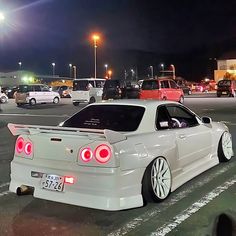 a white car parked in a parking lot next to other cars on the street at night