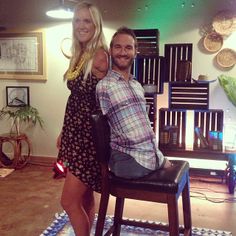 a man and woman pose for a photo in front of a bar stool with their arms around each other