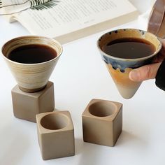 a person is holding a coffee cup in front of three small cups on a table