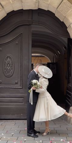 a man and woman are kissing in front of an arch with flowers on the ground