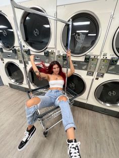 a woman is sitting on a shopping cart in front of washers and drying machines