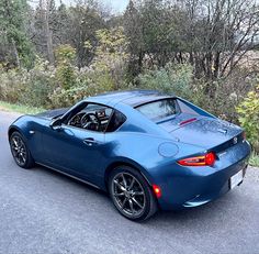 a blue sports car is parked on the side of the road in front of some trees