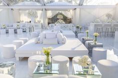 a room with white furniture and flowers in vases on the tables, chairs and couches