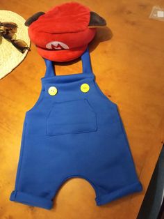 a red hat and blue overalls sitting on top of a wooden table