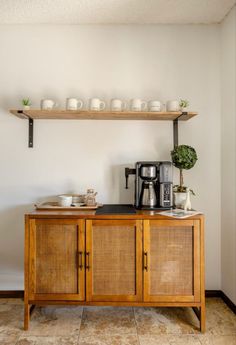 a wooden cabinet with some cups on top of it and a coffee maker next to it