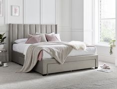 a bedroom with white walls and carpeted flooring has a large gray bed with pink pillows on it