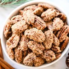 a white bowl filled with nuts next to cinnamon sticks