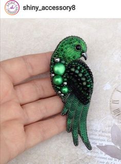 a green bird brooch sitting on top of a person's hand with pearls