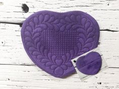 a purple heart shaped pot holder next to a pair of scissors on a white wooden surface