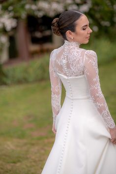 a woman in a white wedding dress standing on grass with her back to the camera