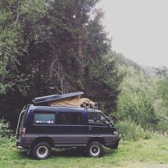 a van with a tent on top parked in the grass next to some trees and bushes