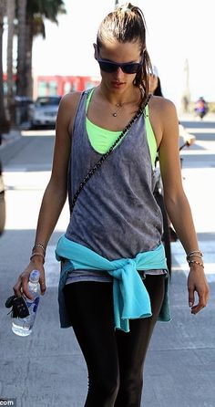 a woman walking down the street with a water bottle in her hand and sunglasses on