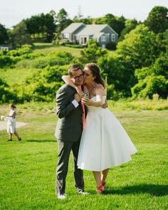 a bride and groom hug in the grass at their wedding ceremony on a farm near some houses