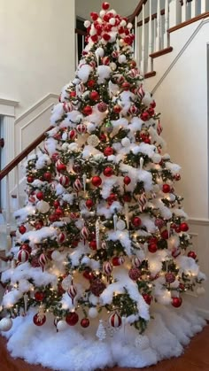 a decorated christmas tree with red and white ornaments on it's bottom, in front of a staircase