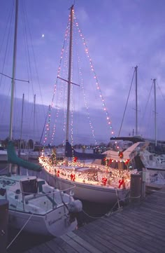 a sailboat is decorated with christmas lights on the deck and in front of other boats