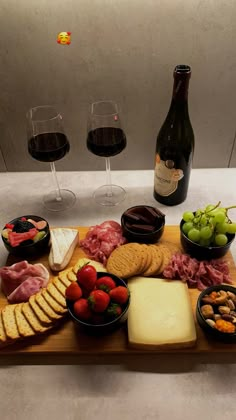 an assortment of cheeses, meats and fruit on a wooden platter with wine glasses