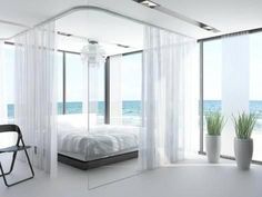 a bedroom with a bed, chair and large windows overlooking the ocean is shown in this image