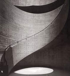 a black and white photo of a curved staircase in a concrete building with sunlight coming through the window