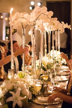 a group of people sitting at a table with flowers and wine glasses on the table