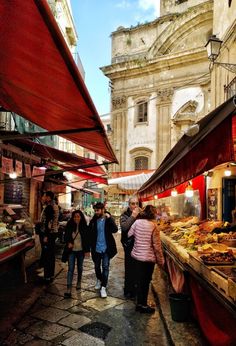 people walking through an open air market with red awnings on the side walk