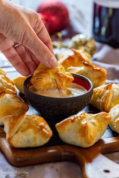 a person dipping some food into a bowl on a cutting board with other pastries in the background