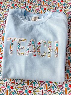 a t - shirt with the word teach embroidered on it sitting on a colorful surface