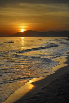 the sun is setting over the water at the beach with waves coming in and people walking on the shore