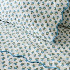 a bed with blue and green floral designs on the coverlet, next to a pillow