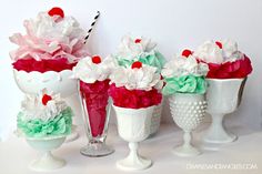 three ice cream sundaes decorated with paper flowers and cherries in vases