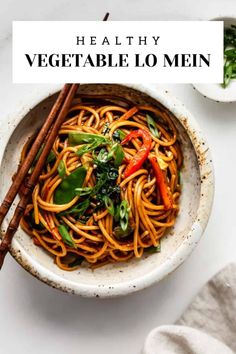 a white bowl filled with noodles and vegetables next to chopsticks on a table