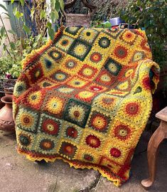 a crocheted blanket sitting on top of a wooden bench next to potted plants