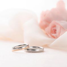 two wedding rings sitting next to each other on top of a white cloth with pink flowers in the background