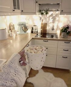 a woman holding a cup of hot chocolate in her hand while sitting at the kitchen counter