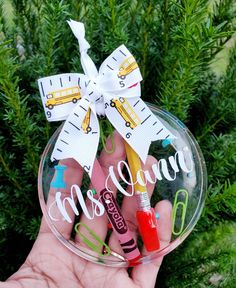 a hand holding a glass ornament with school bus and pencils on it