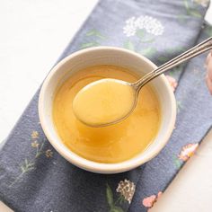 a person is holding a spoon over a bowl of soup on a napkin with flowers