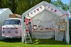 an old vw bus is parked next to a tent with a table and chairs