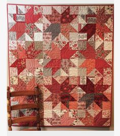 a chair sitting in front of a red and white quilt on a wall next to a wooden rocking chair