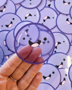 a hand holding a purple button with a face drawn on it and lots of other buttons in the background