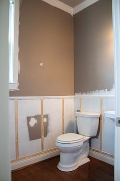 a white toilet sitting inside of a bathroom next to a wall with paint on it