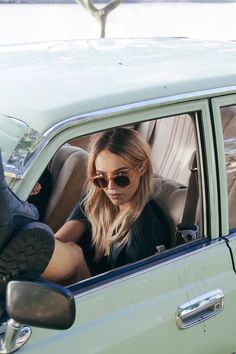 a woman sitting in the passenger seat of a green car with her feet on the steering wheel